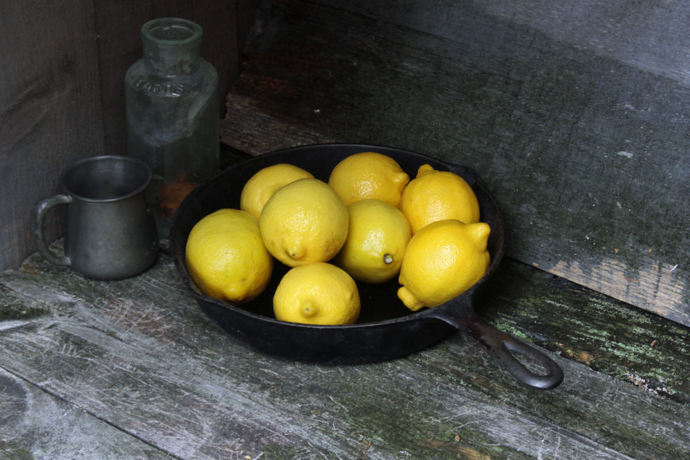 Photo of lemons, cast iron pan, tin cup, glass bottle