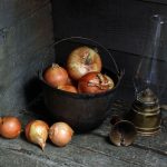 Photo of onions, cast iron pot, antique handbell, and hurricane lamp