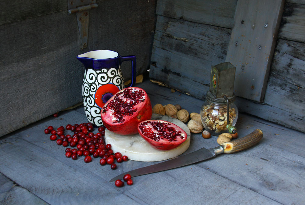Photo of pomegranate, antique nut grinder, ceramic pitcher, cranberries, walnuts